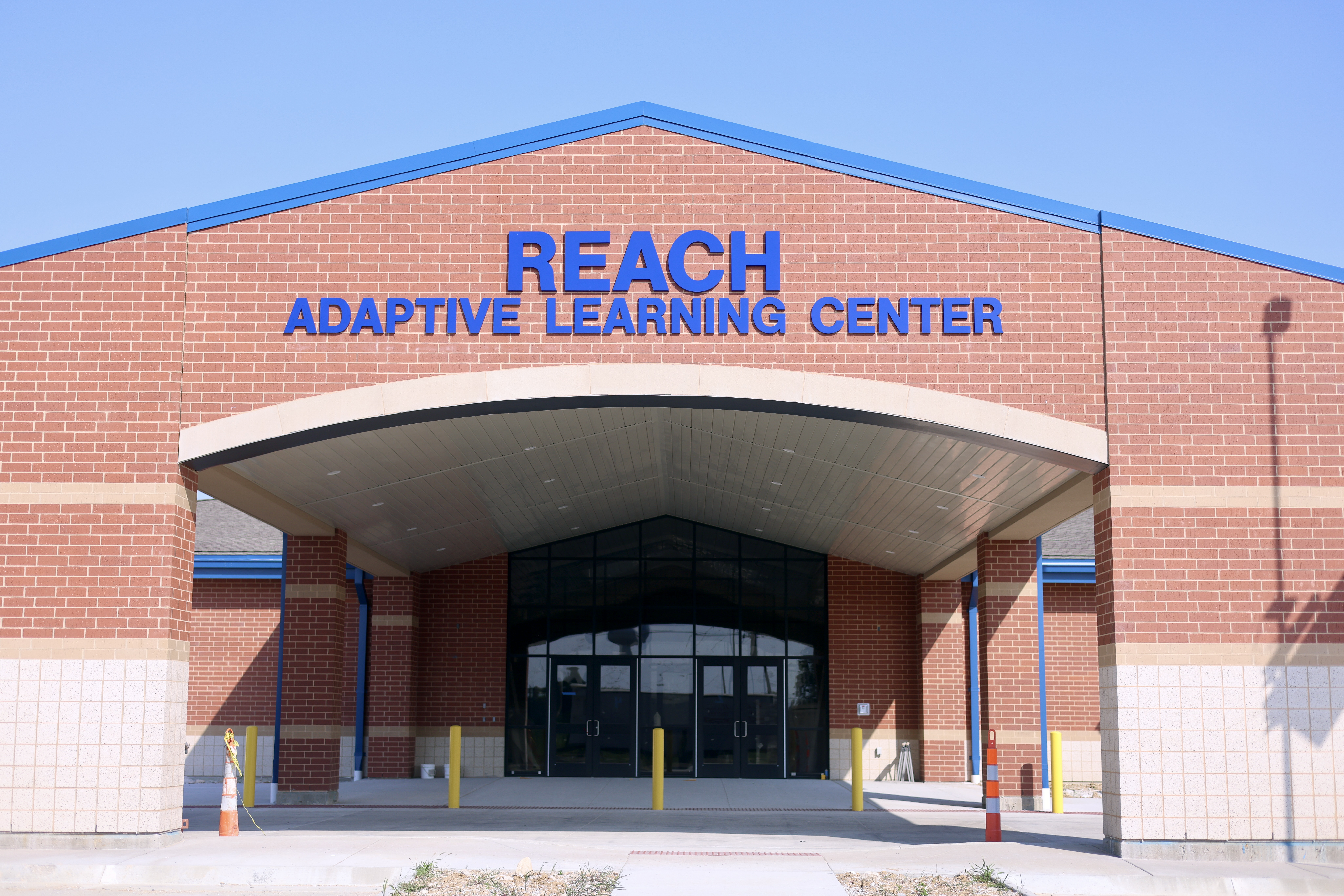 Front entrance of REACH Adaptive Learning Center with blue signage above a covered entrance on a red brick building.