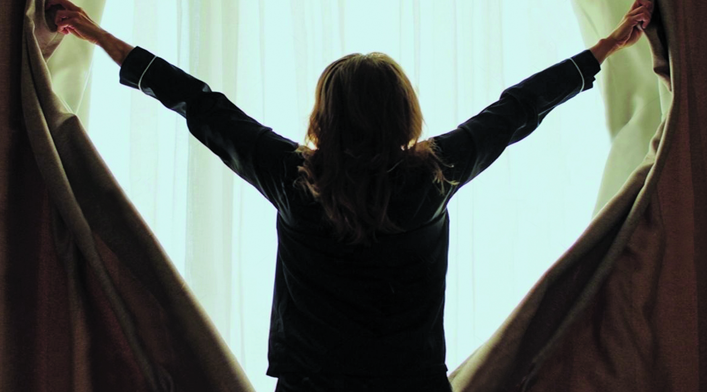 A girl in pajamas opens curtains to reveal a bright, hazy background.