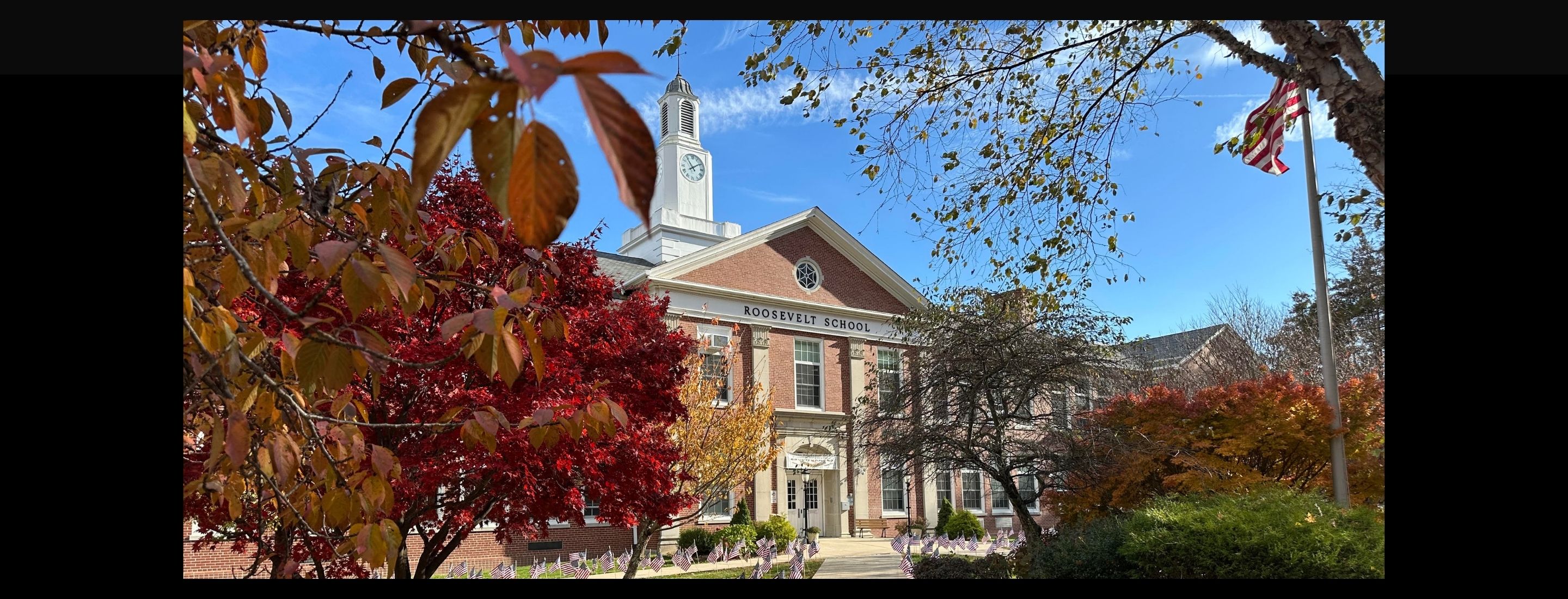 Roosevelt School hidden behind fall foliage. American flags line the sidewalk.