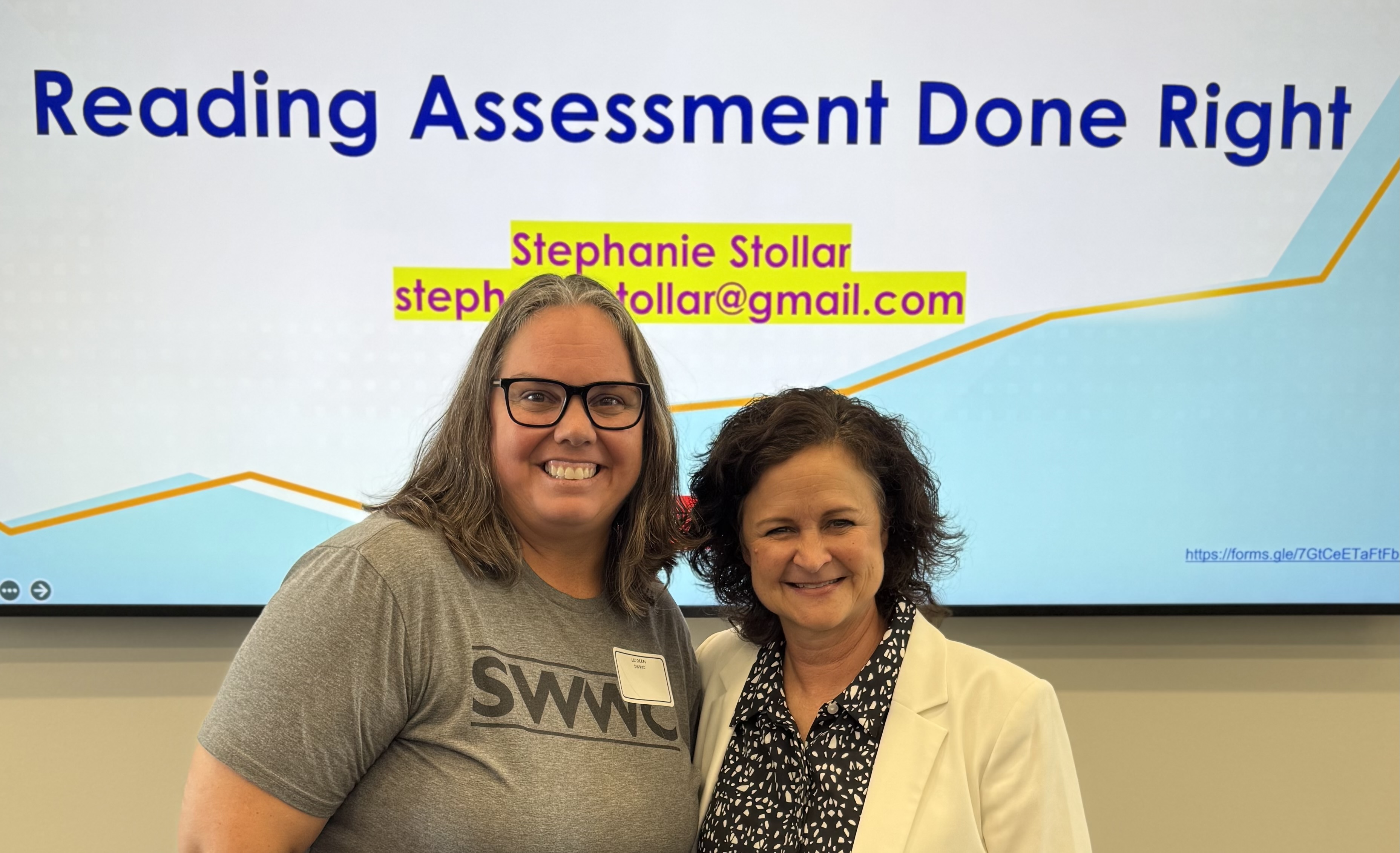 Two smiling women stand in front of a screen displaying "Reading Assessment Done Right" with a graph in the background.