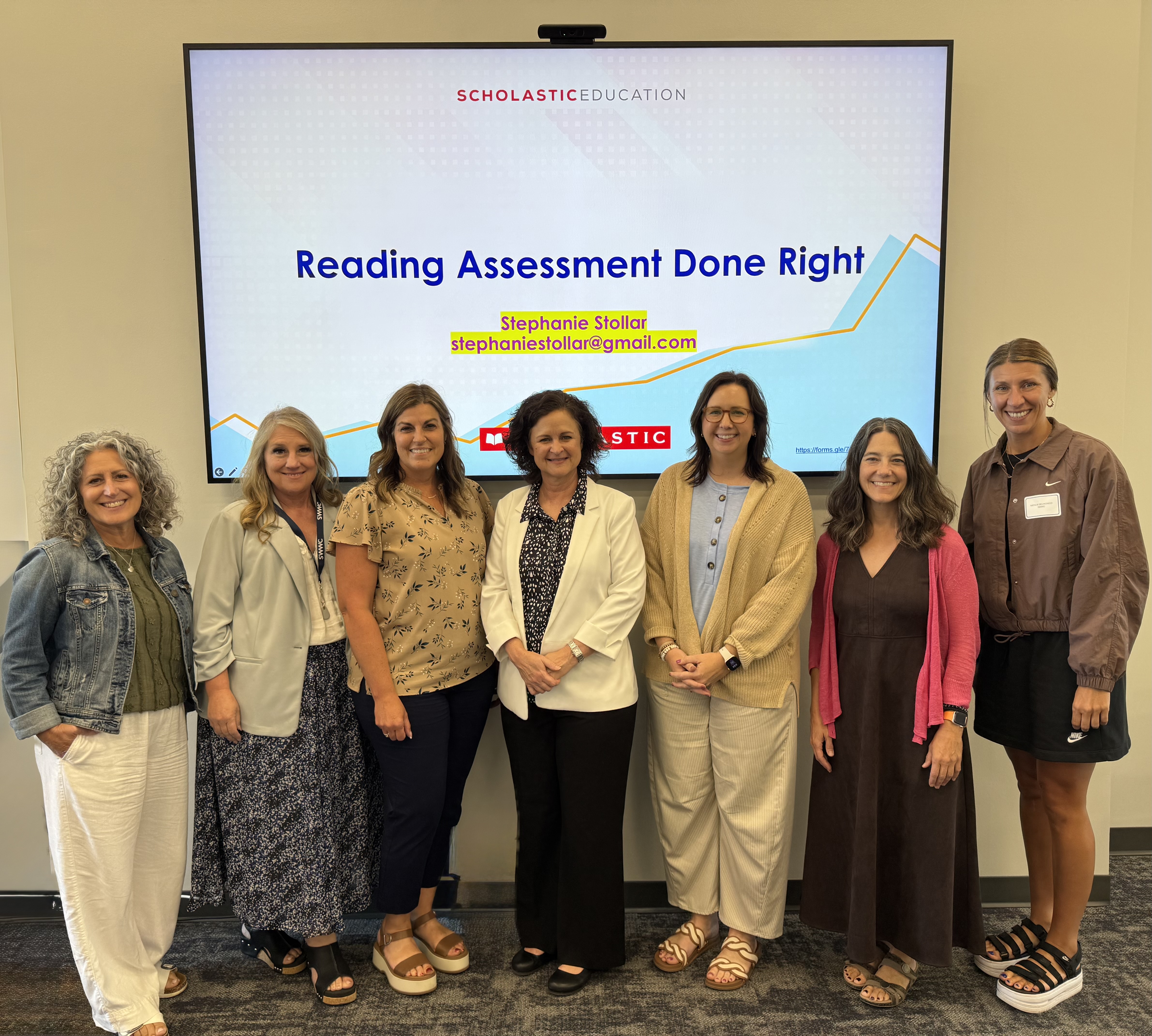 Seven women stand in front of a large screen displaying "Reading Assessment Done Right" with a graph in the background.