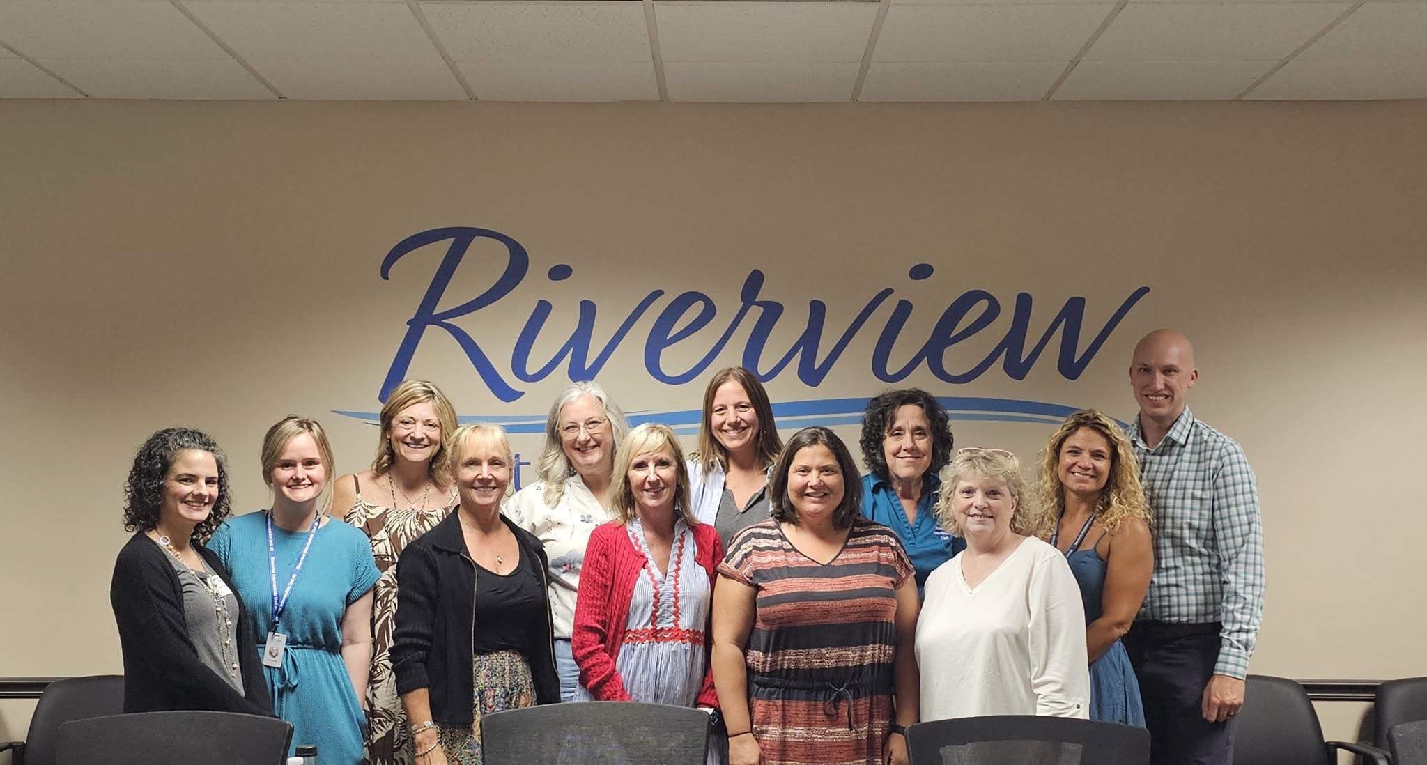 A group of twelve people stand in front of a wall with "Riverview" written on it.