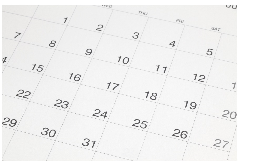 A close-up of a white calendar grid with numbered dates in the foreground against a plain white background.