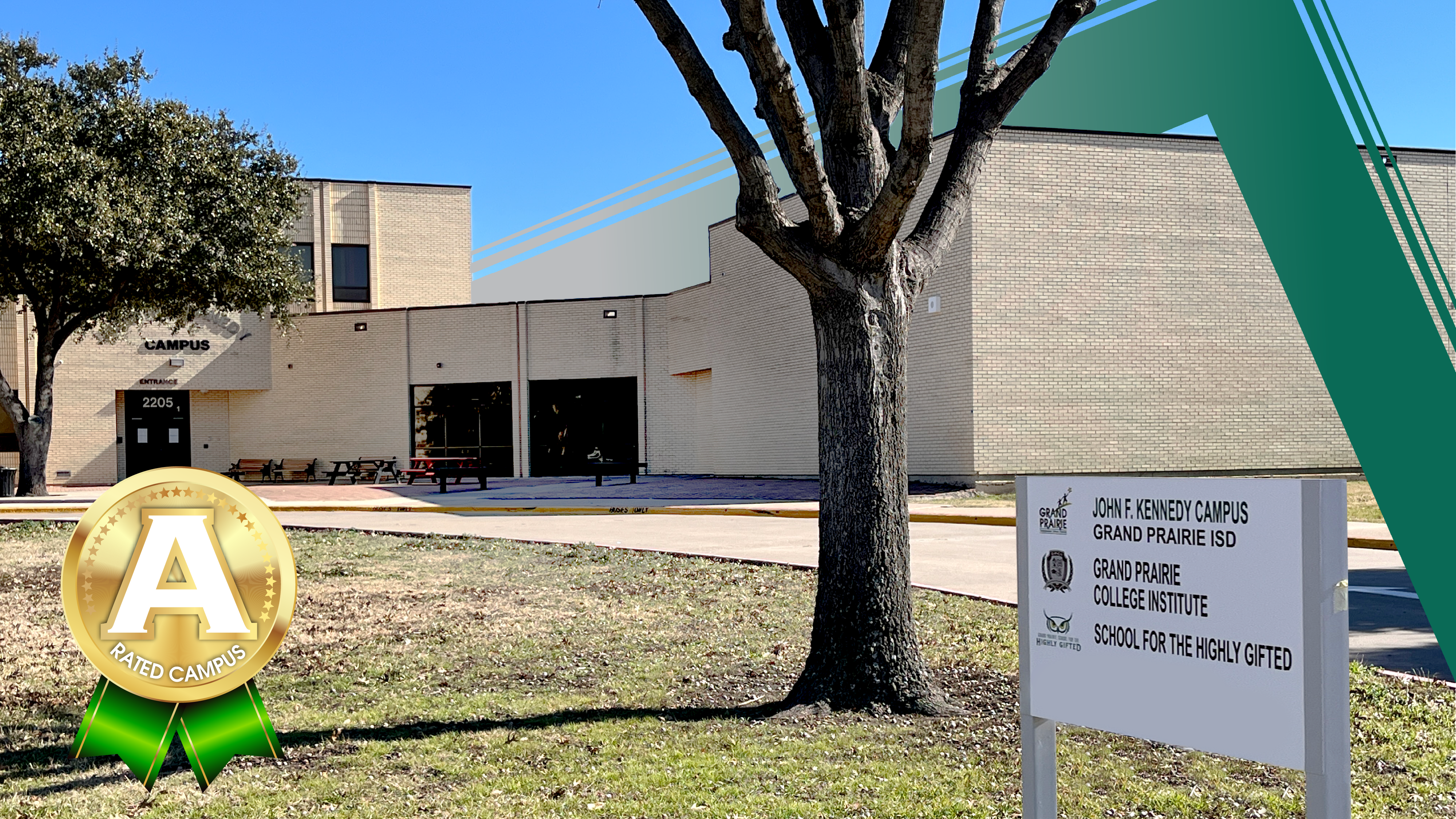 A bare tree stands in the foreground with a brick school building and a sign in the background.