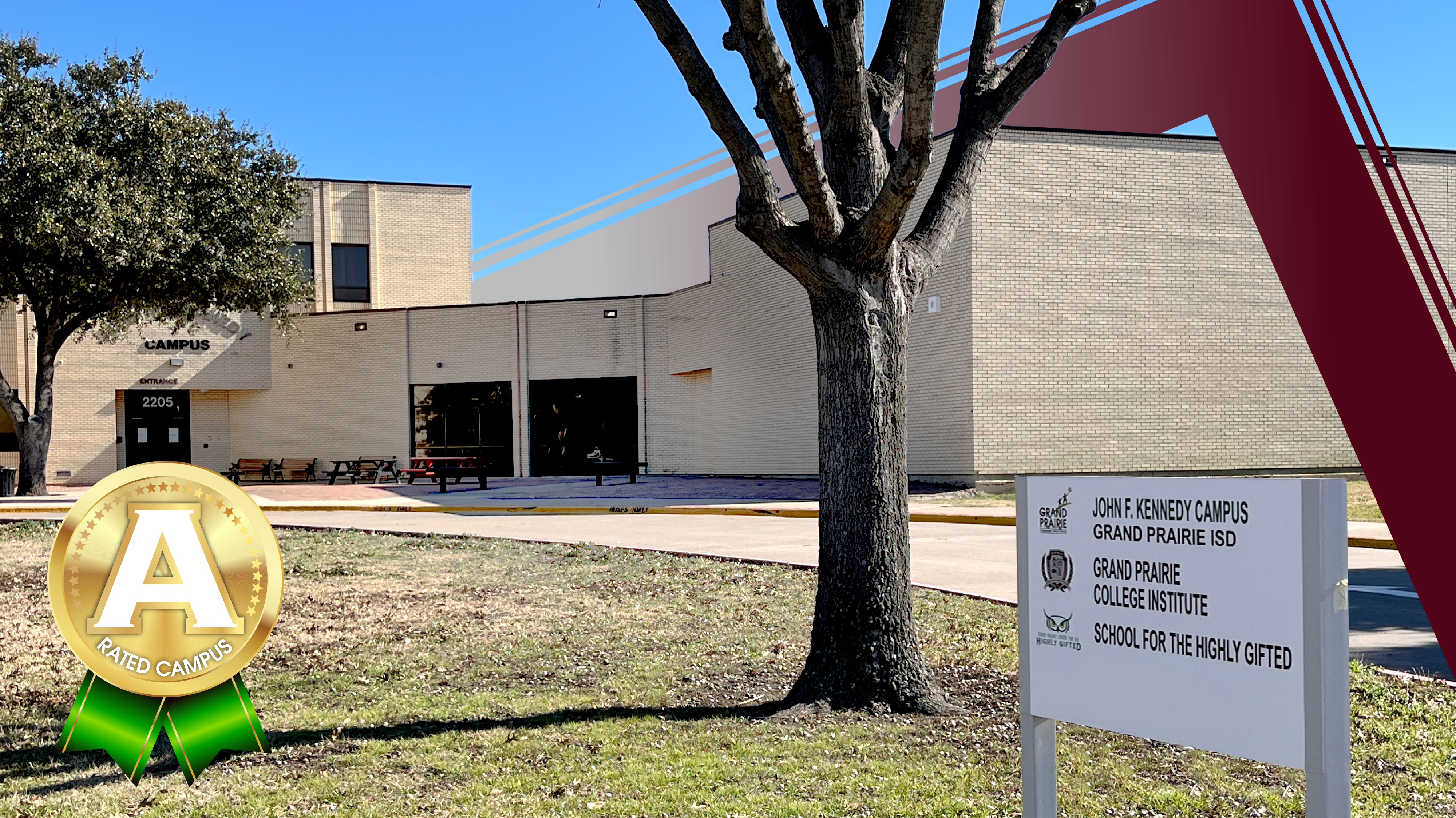A bare tree stands in the foreground with a sign for "John F. Kennedy Campus" and an "A" award, while a tan brick school building with large windows forms the background.