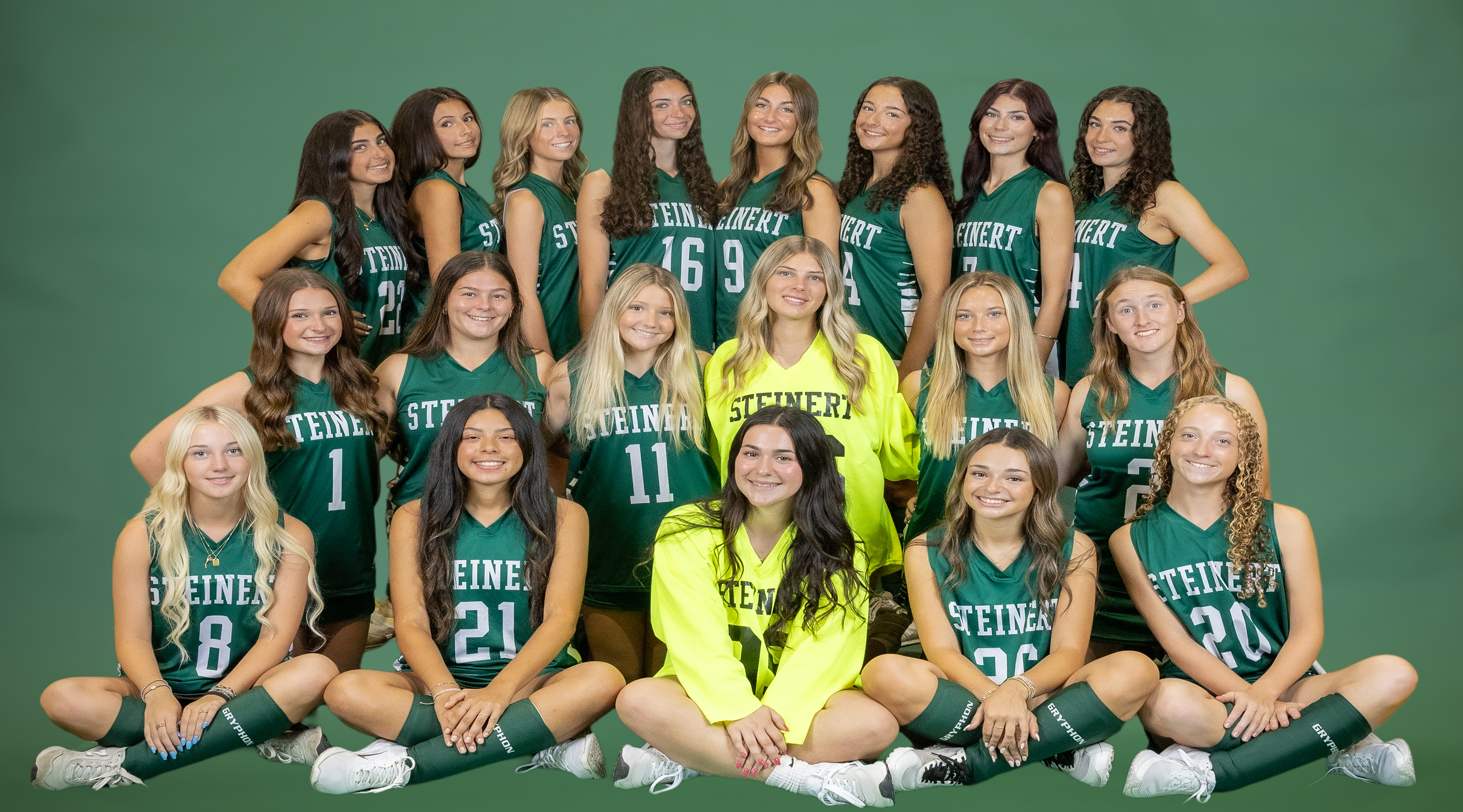 A group of young women in green and white uniforms pose for a photo in front of a green backdrop.