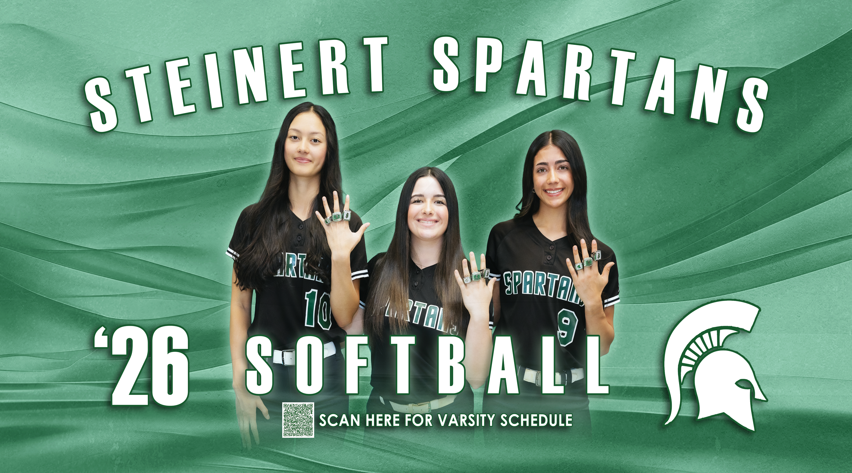 Three young women in softball uniforms stand in the foreground, proudly displaying their championship rings, against a green, wavy background with the text "STEINERT SPARTANS SOFTBALL" and a Spartan helmet logo.