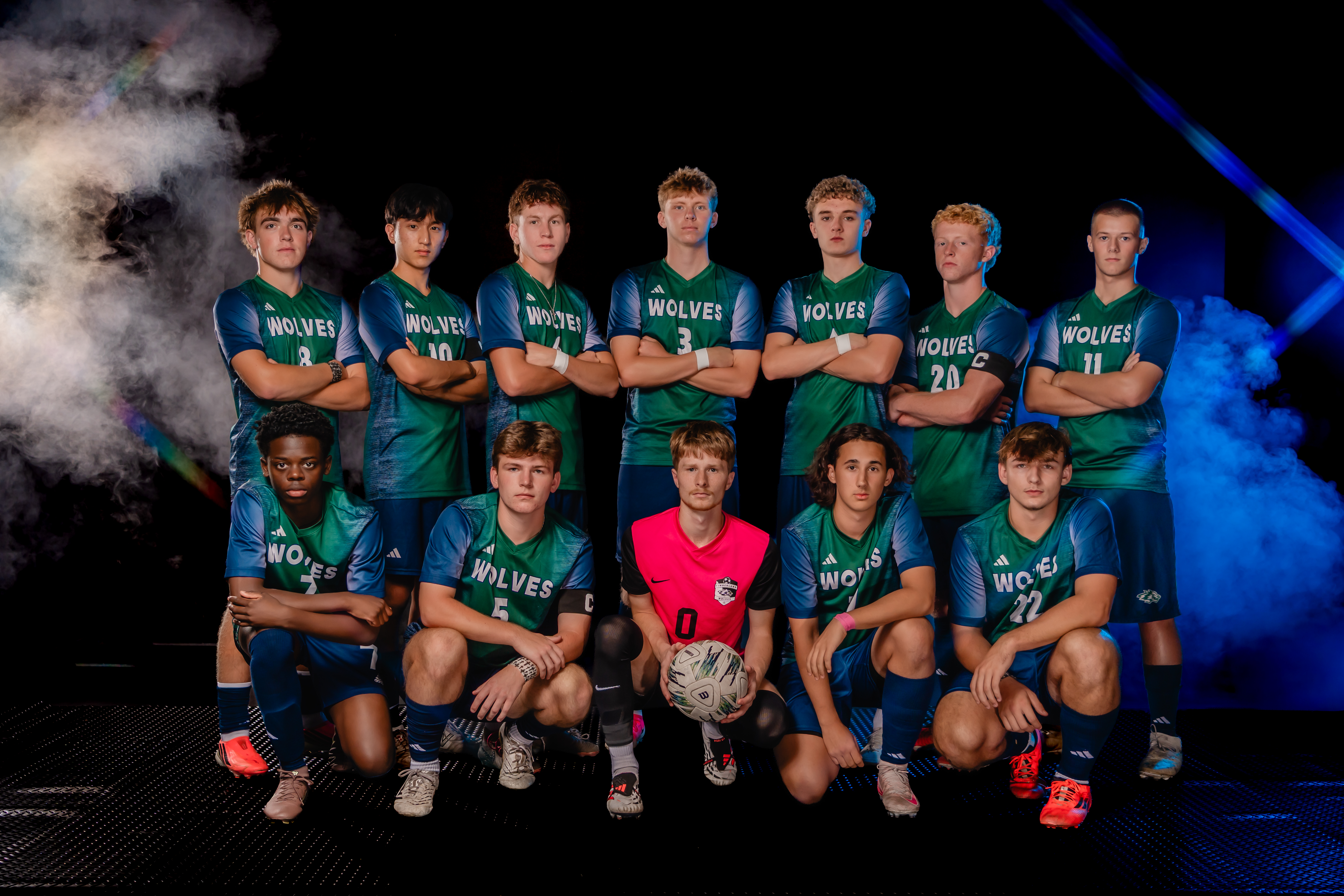 A soccer team in green and blue uniforms poses for a group photo against a dark background filled with dramatic smoke and blue lighting.
