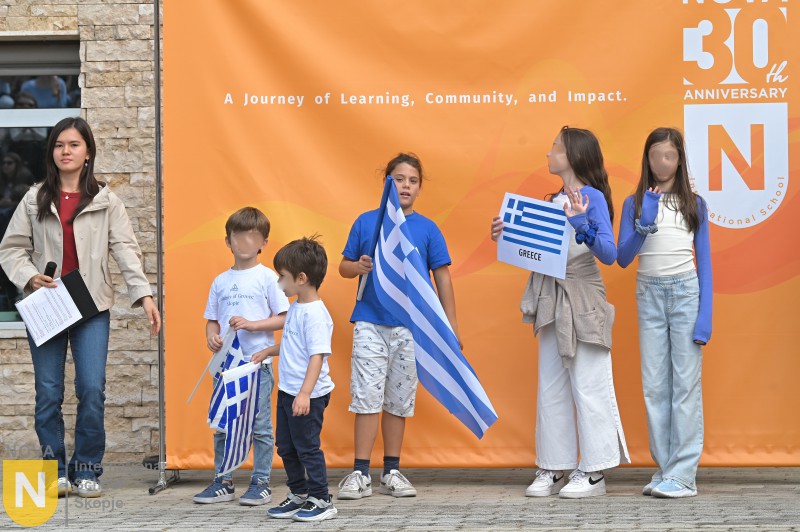 Students holding the Greek flag in front of the NOVA 30th anniversary banner